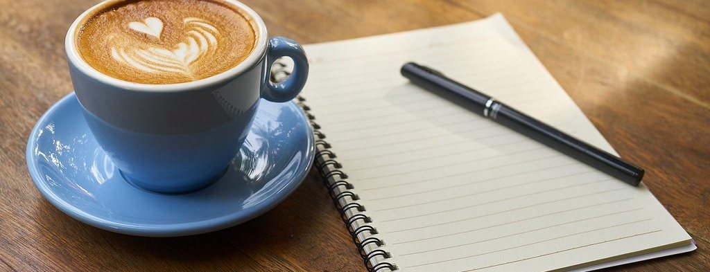 A cup of coffee beside an open notebook and pen